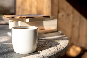 white cup with cappuccino coffee and books on an old table with a background of old rustic woods