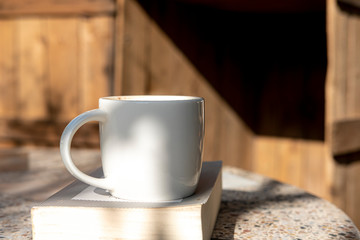 white cup with cappuccino coffee and books on an old table with a background of old rustic woods