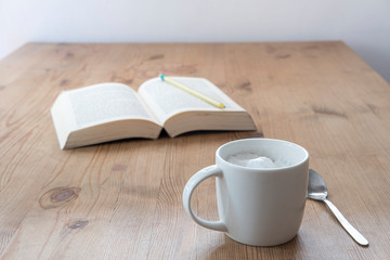 cup with coffee and a open book on a rustic wooden table
