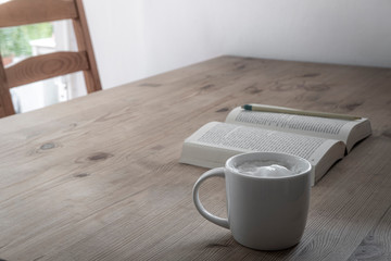 cup with coffee and a open book on a rustic wooden table