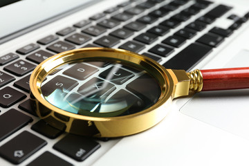 Magnifying glass on keyboard of modern laptop, closeup. Search concept
