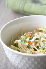 Healthy coleslaw salad with cabbage, carrots, dill and white dressing sauce in a white bowl on wooden surface