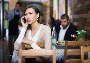 sad female in restaurant talking mobile phone