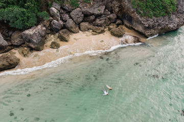 Fototapeta na wymiar Beach drone view tropical island, white beach with waves, couple lying on the back in water and holding hands. Aerial Photo.