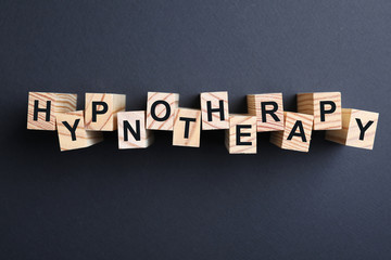 Wooden blocks with word HYPNOTHERAPY on black background, flat lay