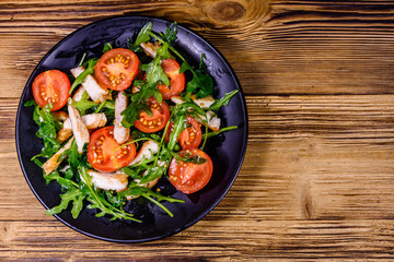 Roasted chicken breasts and salad with arugula and cherry tomatoes in a ceramic plate. Top view