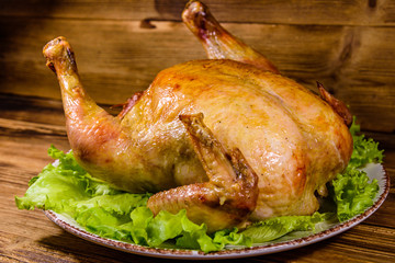 Plate with roasted whole chicken and lettuce leaves on a wooden table