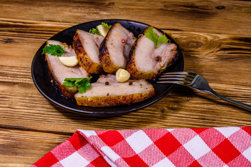Slices of baked pork belly, garlic and parsley on a black plate