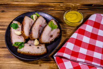 Slices of baked pork belly, garlic and parsley on a black plate