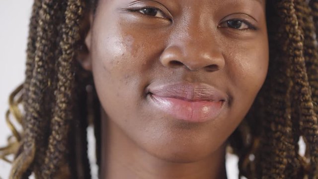 Extreme close up shot of beautiful black woman with dreadlocks putting moisturizing lotion on her cheek and smiling for camera