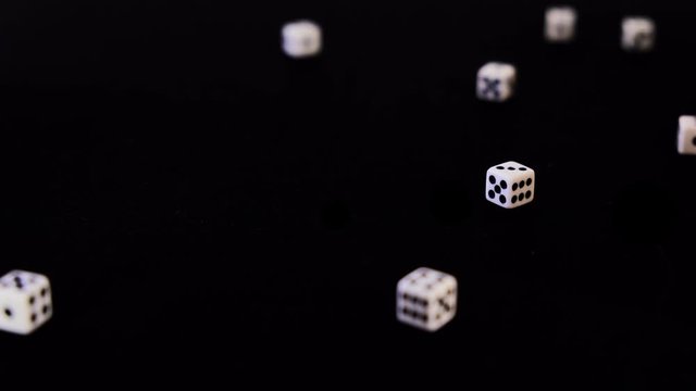 Falling, flying out white cubes on a black background. Dice fall, rotate and bounce on a black surface. Stops in sight. Concept of business and casino or gambling. Close-up.