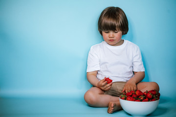Toddler boy sitting with bowl of strawberries on the blue background