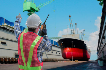 worker in Shipyard with walkie talkie in hand speaking radio communication receiver, surveyor, inspecting the final repairing man front ship moored in floating dry dock background.