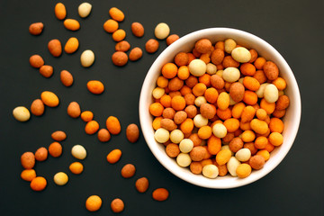 Peanuts with a crispy crust around it in a white bowl on a black metallic surface