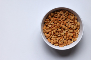 Peanuts in a white bowl on a white background, seen from above, with copy space