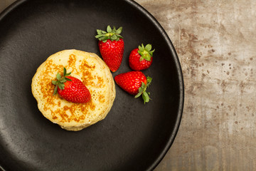 Tortitas con fresas sobre un plato redondo negro sobre un fondo gris de metal rústico. Vista superior. Copy space