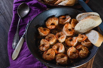 Fried prawns in a pan on a table with bread, farm serving food, dark background. The concept of nutrition and beautiful serving of food
