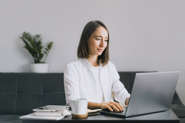 Young woman sitting at the table and using laptop, texting and surfing internet.