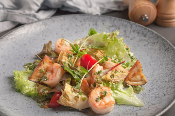 Restaurant menu. Warm salad with tomatoes, king prawns, eggplant and lettuce. Micro-village. Blue plate.Red, orange, green, yellow