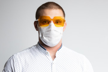 Male office worker in polo shirt, medical mask and bright sunglasses on a white isolated background. Concept photo: worker is afraid of news about coronovirus and believes in positive