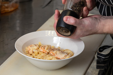 Step by step cooking chicken: a man sprinkles black pepper from a special jar on a plate with cooked pasta with cheese, shrimp and cream sauce