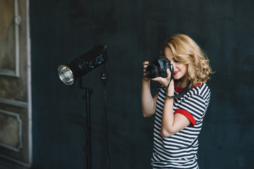 Young beautiful woman photographer with a camera in her hands works in a photo studio using artificial lighting. Women's work is a hobby. Soft selective focus.