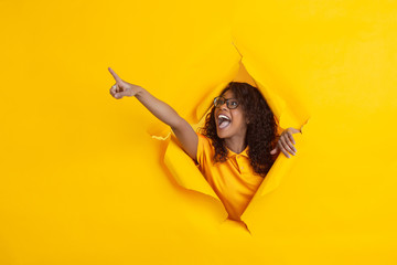 Crazy happy pointing. Cheerful african-american young woman in torn yellow paper background,...