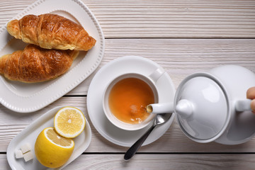 Top view of pouring tea on a cup with lemon and croissants on white table