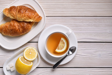Top view of a cup of tea with lemon and croissants on white table