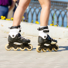 Beautiful female legs in roller skates on the embankment of the river on a summer sunny day.