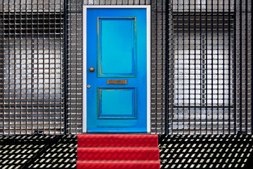 Manipulated photo of a red carpet leading to a building with a blue door and bricked-up windows behind a security fence. Usable for security, protection or insurance concepts