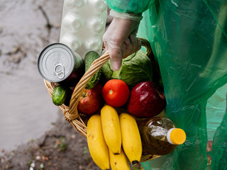 Basket of food in the hands of a female volunteer, close-up. Delivery of volunteer assistance in rainy weather.
