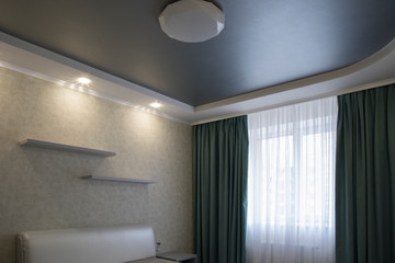 Interior of a small cozy bedroom with furniture and curtains and grey ceiling