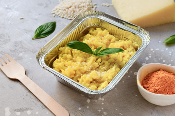 food delivery risotto milanese takeaway in an aluminum container. ingredients for the risotto  yellow recipe. delivery from the restaurant to order. rice, cheese, Basil, spices top view airline meals