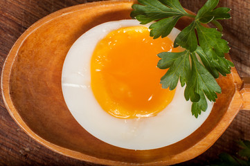 Boiled egg in a wooden spoon on a board