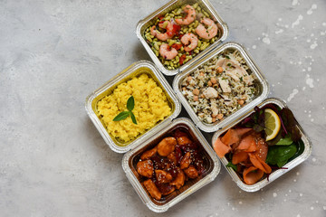 Food delivery. Different aluminium lunch box with healthy food risotto, chicken with chickpeas and rice, salmon and spinach, chicken teriyaki, shrimp and green beans. airline meals snacks. takeaway
