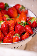 Ripe strawberries in white colander standing under pouring water in sink