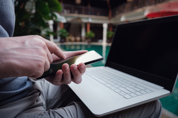 travel blogger sitting at swiming pool writing article on white laptop.