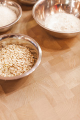 Metal bowls with oatmeal, flour and sugar on a wooden table