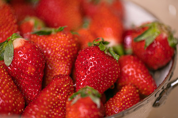 Ripe strawberries in white colander standing under pouring water in sink