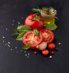 Fresh basil leaves with tomatoes, olive oil, rosemary and garlic on black stone background.