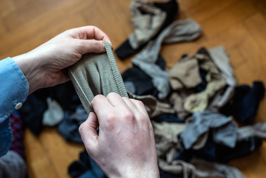 Heap of old socks as a symbol of old life, clutter, fast fashion, consumerism and nostalgic past. Male hands holding an old sock. Concept of tidying the mess