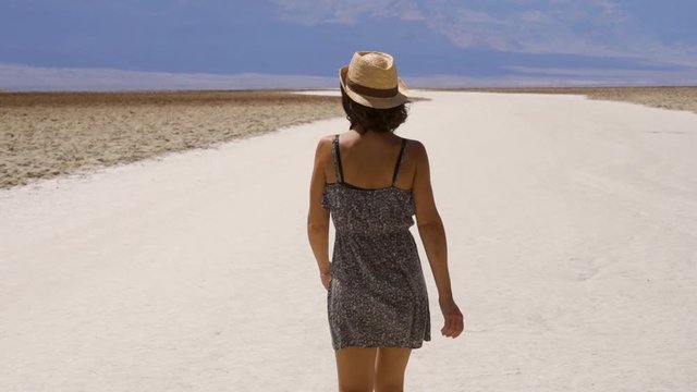 A young woman in a dress and hat walking in Badwater Basin in the desert of Death Valley, California. United States
