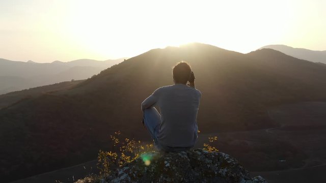 Concept of achievement and illumination at the end of the path as a reward for the fight A man sitting on top of a cliff watches the sunset in the mountains