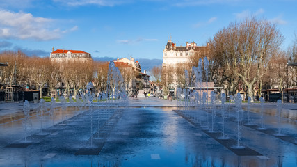 Béziers in France, the Jean-Jaures place, typical facades in the old center, with water jets in a public park
