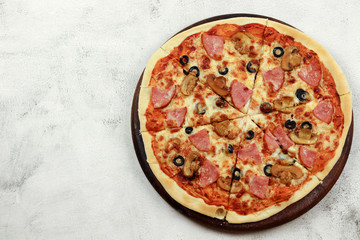 Pizza with ham, olives and mushrooms on a wooden cutting board on a light gray background. Top view, flat lay