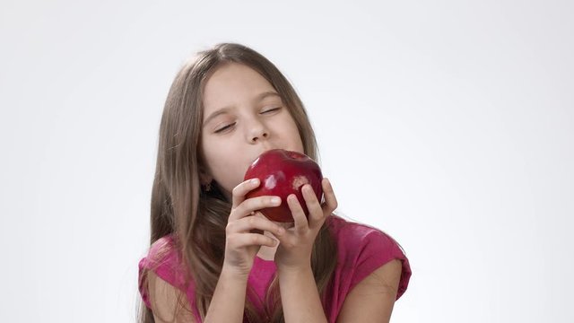 Little girl on white eats a big red apple. A girl bites a piece of red ash and tastes it.
