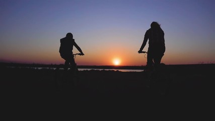 Two bikers riding their mountain bicycles along river in amazing rays of sunset. Sport and healthy lifestyle concept