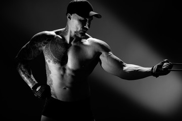 Fototapeta na wymiar Handsome muscular man with tattoo pulls rubber bands in gym. Athlete trains. Healthy lifestyle, fitness workout. Black and white photo