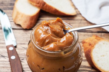 Boiled condensed milk with a glass jar on a wooden background. Sweet paste spread on slices of...